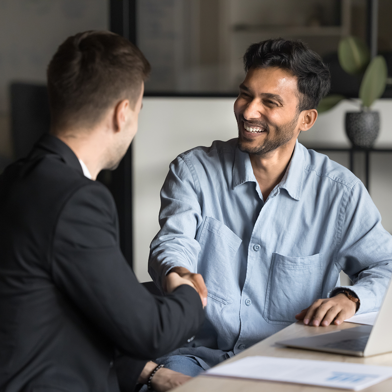 Cheerful male business partners shaking hands at workplace table